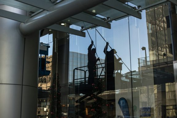 Deux personnes nettoient des vitres sur un échafaudage, reflet sur la façade.