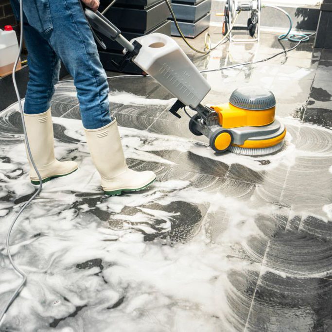 Un technicien de nettoyage de la société de nettoyage 74 NETT utilise une monobrosse pour décrasser et nettoyer un sol carrelé d'un magasin 